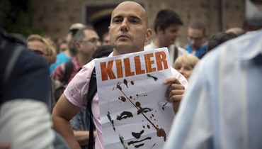 متظاهر يحمل ملصقًا يصوّر بوتين مع تعبير "قاتل" خلال مسيرة احتجاجية أمام مبنى الرئاسة البلغارية وسط صوفيا (10 آب 2022، أ ب).  
