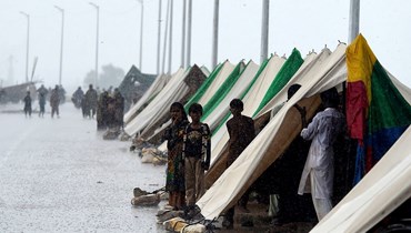 أشخاص فروا من منازلهم التي ضربتها الفيضانات، يقفون خارج خيام مؤقتة أقيمت على طريق خلال هطول الأمطار في سوكور بإقليم السند (27 آب 2022، أ ف ب).