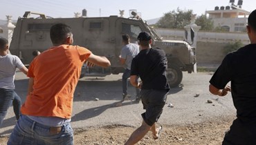 شبان فلسطينيون يرشقون بالحجارة سيارة جيب للجيش الإسرائيلي في بلدة سلواد قرب رام الله في الضفة الغربية المحتلة، بعد عملية عسكرية في البلدة (31 آب 2022، أ ف ب). 