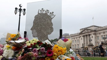 صورة للملكة إليزابيث إلى جانب باقات من الزهر مقابل بوابة قصر بكنغهام حداداً على رحيلها (أ ف ب).