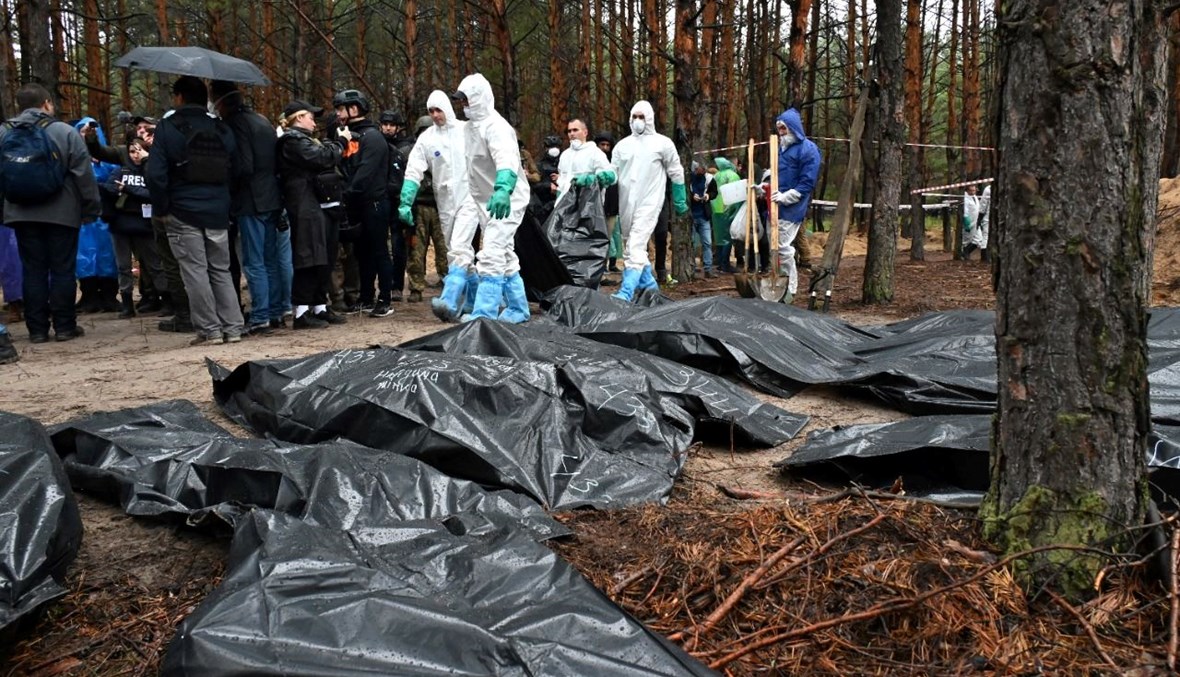 محققون يحملون كيسًا للجثث بينما بدت أكياس أخرى ملقاة على أرض غابة قرب إيزيوم شرق أوكرانيا (23 أيلول 2022، أ ف ب). 