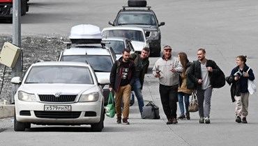 أشخاص يمرون قرب مركبات تحمل لوحات ترخيص روسية توقفت عند الجانب الجورجي لنقطة التفتيش الجمركية فيركني لارس بين جورجيا وروسيا (25 أيلول 2022، أ ف ب). 