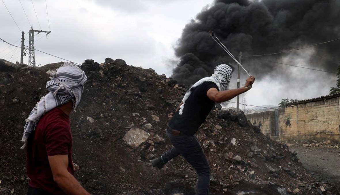 فلسطينيّان يقذفان الحجارة خلال اشتباكات مع جنود إسرائيليين في الضفة الغربية المحتلة (7 ت1 2022، أ ف ب).