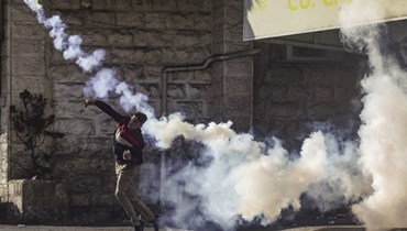 متظاهر فلسطيني يعيد قنبلة غاز مسيل للدموع باتجاه الجيش الإسرائيلي خلال مواجهات في وسط مدينة الخليل بالضفة الغربية المحتلة (أ ف ب).