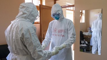 طبيبان باللباس الواقي يصليان معاً قبل زيارة مريض كان على اتصال بإحدى ضحايا الإيبولا، في قسم العزل بمستشفى عنتيبي في عنتيبي بأوغندا (20 ت1 2022، أ ب). 