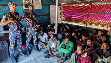 لاجئون من الروهينغا محتجزون جلسوا قرب عناصر من أفراد الأمن بعد حملة مداهمات في مخيم الروهينغا في أوخيا (28 ت1 2022، أ ف ب). 