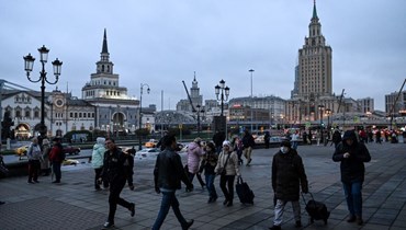 اشخاص يمشون في ساحة قبالة ناطحة سحاب من عهد ستالين في موسكو (29 ت1 2022، أ ف ب).