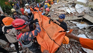 عمال إنقاذ يحملون جثة ضحية في سيانجور بعد الزلزال (22 ت2 2022، أ ف ب).  