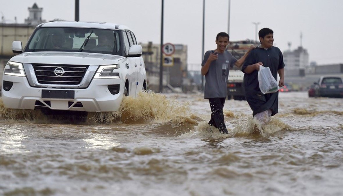 شخصان يعبران شارعا غمرته المياه بعد هطول أمطار غزيرة في مدينة جدة (24 ت2 2022، أ ف ب). 