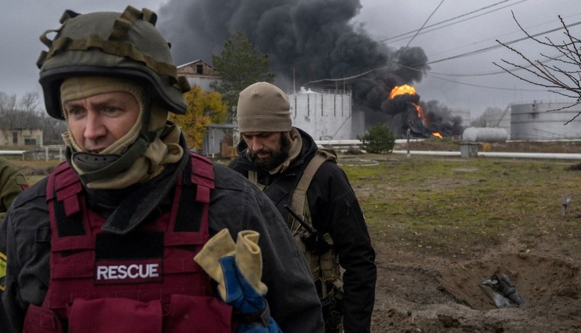عنصر من خدمة الإنقاذ الأوكراني وجندي يتفقّدان المنطقة مع تصاعد الدخان الأسود بعد هجوم على احتياطي نفطي في خيرسون (20 ت2 2022 - أ ف ب).