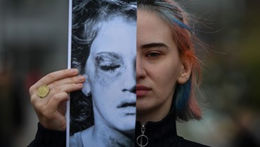 ناشطة نسويّة ترفع صورة لوجه امرأة ضحية عنف ذكوريّ خلال مسيرة في بوخارست (4 آذار 2020 - أ ف ب).