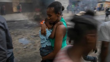 أم تحمل ابنها أمام حاجز مشتعل أثناء احتجاج ضد الحكومة في هايتي، في 18 تشرين الثاني (أسوشيتد برس).
