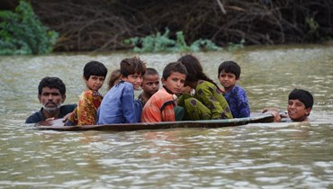 صورة ارشيفية- رجل وفتى يستخدمان طبق قمر صناعي لنقل أطفال في منطقة غمرتها الفيضانات بعد هطول أمطار موسمية غزيرة في جعفر أباد بمقاطعة بلوشستان (26 آب 2022، أ ف ب). 