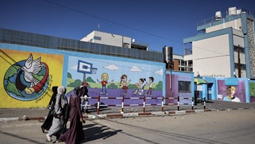 نساء فلسطينيات يمرن قرب مدرسة تديرها الأونروا في غزة (1 ك1 2022، أ ف ب). 