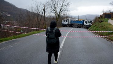 امرأة تمشي باتجاه حاجز أقامه الصرب العرقيون على طريق في قرية روداري قرب بلدة زفيكان بكوسوفو، باستخدام شاحنات (12 ك1 2022، ا ف ب). 