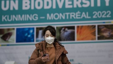 امرأة تتفحص هاتفها وخلفها لافتة لمؤتمر الأمم المتحدة للتنوع البيولوجي (COP15) في مونتريال بكيبيك (17 ك1 2022، أ ف ب). 