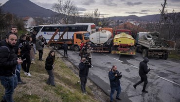 صحافيون يتابعون صرب كوسوفو وهم يبعدون شاحنات بعدما وضعوها حاجزا على الطريق في قرية روداري قرب بلدة زفيكان (29 ك1 2022، أ ف ب).