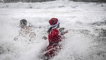 امرأة ترتدي زي بابا نويل تحتفل بيوم رأس السنة الجديدة في المياه المتجمّدة في منطقة لشبونة (أ ف ب). 