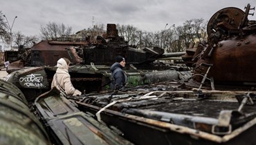اشخاص يمرون بين مركبات عسكرية روسية مدمرة معروضة في الهواء الطلق في كييف (5 ك2 2023، أ ف ب). 