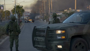 جنود مكسيكيون يقفون على مقربة من مركبات مشتعلة في أحد الشوارع خلال عملية لاعتقال أوفيديو غوسمان في كولياكان بولاية سينالوا بالمكسيك (5 ك2 2023، أ ف ب). 