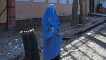 امرأة بالبرقع تقف بجانب كيس من الفحم تبرع به فريق تطوعي في كابول (13 ك2 2023، أ ف ب).