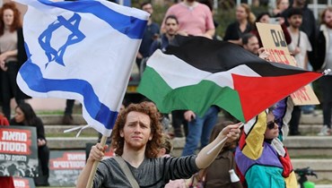 طالب إسرائيلي يرفع العلمَين الفلسطيني والإسرائيلي خلال تظاهرة مناهضة لحكومة نتنياهو في تل أبيب (أ ف ب).