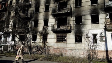 امرأة تمر قرب مبنى سكني مدمر في بلدة سيفيرودونيتسك الخاضعة للسيطرة الروسية في منطقة لوغانسك الشرقية (24 ك2 2023، أ ف ب). 