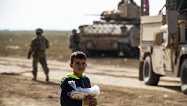 طفل يحمل كيس خبز على طريق بينما قام رتل أميركي بدوريات في المنطقة القريبة من بلدة تل حميس جنوب شرق القامشلي بمحافظة الحسكة شمال شرق سوريا (26 ك2 2023، أ ف ب).