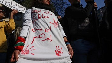 أحد أقارب أحد ضحايا انفجار مرفأ بيروت يحمل لافتة كتب عليها "لن ننسى جريمتك" خلال مسيرة خارج قصر العدل (أ ف ب). 