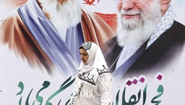 امرأة إيرانية تمشي أمام ملصق يحمل صور مؤسس الجمهورية الإسلامية الراحل آية الله روح الله الخميني والزعيم الإيراني الأعلى آية الله علي خامنئي (أ ف ب). 