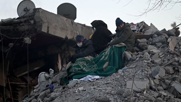 يجلس الأقارب فوق أنقاض المباني المنهارة، حيث تواصل فرق الإنقاذ البحث عن الضحايا والناجين، بعد زلزال قوته 7.8 درجة ضرب المنطقة الحدودية بين تركيا وسوريا (أ ف ب). 
