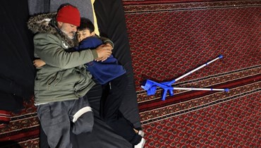 رجل فقد أفراد عائلته في الزلزال يعانق ابنه فيما لجأ نازحون سوريون إلى مسجد السلطان إبراهيم في بلدة جبلة غرب دمشق (12 شباط 2023، أ ف ب). 