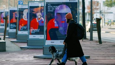 امرأة تمشي مع كلبها قرب ملصقات دعائية لمهرجان برلين السينمائي الدولي الـ73 في برلين (15 شباط 2023ـ أ ف ب). 