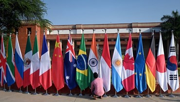  رجل يرتّب الأعلام الوطنية للدول المشاركة خلال اجتماع وزراء خارجية مجموعة العشرين في نيودلهي (أ ف ب). 