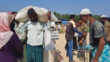 لاجئون من الروهينغا يحملون مواد إغاثة بعد تسلمها عند نقطة توزيع في مخيم كوتوبالونغ للاجئين في أوخيا (2 آذار 2023، أ ف ب).