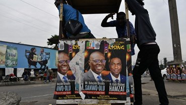 أشخاص اتكأوا على منصة وضعت عليها ملصقات انتخابية في لاغوس (7 آذار 2023، ا ف ب). 
