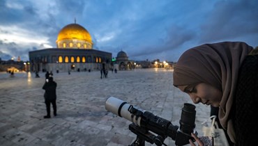 امرأة تنظر عبر التلسكوب الى القمر قرب قبة الصخرة في مجمع المسجد الأقصى في البلدة القديمة بالقدس للاحتفال ببداية شهر رمضان المبارك (21 آذار 2023، أ ف ب). 