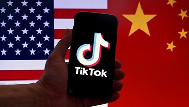 شعار TikTok معروضًا على شاشة جهاز iPhone أمام العلمين الأمريكي والصيني (أ ف ب).
