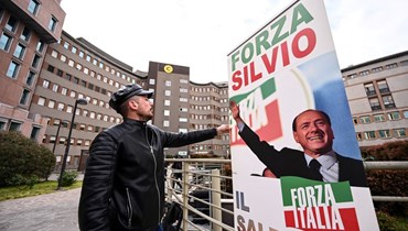 رجل وضع لافتة  لبرلوسكوني أمام مستشفى سان رافاييلي في ميلانو حيث تم إدخاله للعلاج (7 نيسان 2023، أ ف ب). 