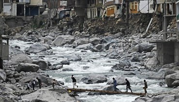 يعبر السكان جسراً موقتاً بالقرب من الفنادق والمنازل الفارغة التي تضررت من الفيضانات المفاجئة على ضفاف نهر سوات الصيف الماضي (أ ف ب). 