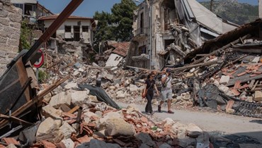 أشخاص يسيرون بين أنقاض المباني التي دمّرها الزلزال، خلال الانتخابات الرئاسية والبرلمانية، في أنطاكيا (14 أيار 2023 - أ ف ب).