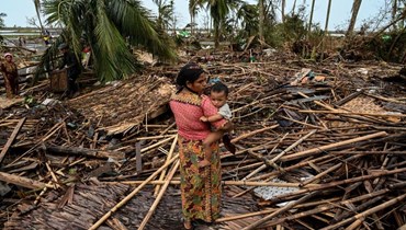  امرأة تحمل طفلها بجوار منزلها المدمّر بعد أن ضرب إعصار موكا اليابسة (أ ف ب). 