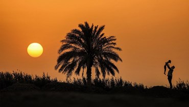 رجل يحمل صبياً وهو يقف بجانب شجرة نخيل عند غروب الشمس على مشارف مدينة الناصرية جنوب العراق (أ ف ب). 
