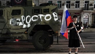 رجل يحمل العلم الوطني الروسي أمام مركبة عسكرية تابعة لمجموعة فاغنر مع لافتة كُتب عليها "روستوف"، في روستوف-أون-دون (24 حزيران 2023 - أ ف ب).