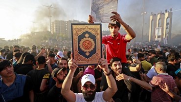 أحد أنصار التيار الصدري العراقي يرفع القرآن أمام السفارة السويدية في بغداد (30 حزيران 2023، ا ف ب). 