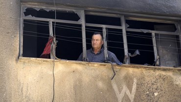 رجل ينظر من النافذة المحطمة لمبنى في مخيم جنين بالضفة الغربية المحتلة (أ ف ب).