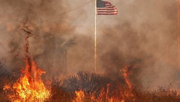 النيران تحيط العلم الأميركي في وادي مورينو في مقاطعة ريفرسايد، كاليفورنيا، التي شهدت حريقاً هائلاً (14 تموز 2023 - ا ف ب).