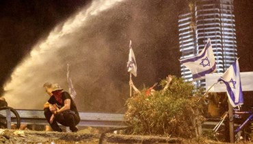  متظاهرون يجلسون في وجه خراطيم المياه التي أطلقتها شرطة مكافحة الشغب الإسرائيلية خلال احتجاج على مشروع قانون الإصلاح القضائي للحكومة الإسرائيلية في تل أبيب (أ ف ب). 