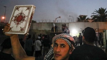 متظاهر أمام السفارة السويدية في بغداد يرفع نسخة من القرآن الكريم (أ ف ب).