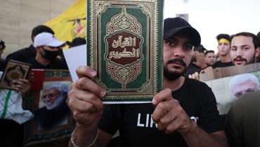 متظاهر عراقي يرفع القرآن الكريم أمام السفارة السويدية في بغدادا (أ ف ب).
